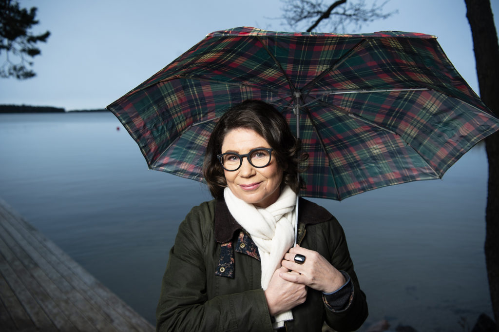 Marjo Heiskanen - kirjailija sateenvarjon alla meren rannassa